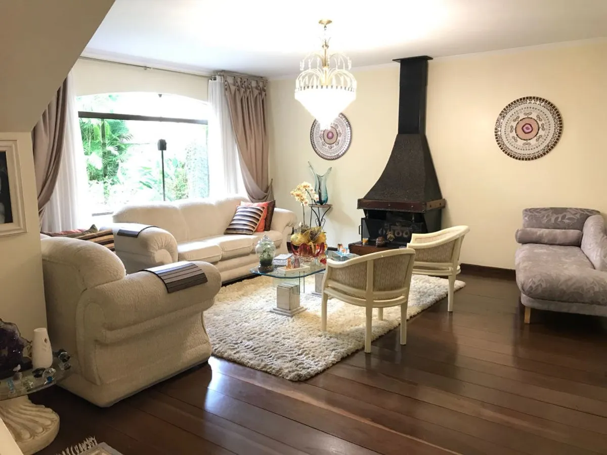 Sala de estar clássica com sofás bege, lustre de cristal, lareira preta e piso de taco, antes da reforma