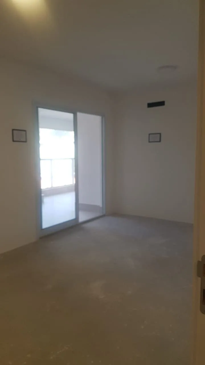 Cômodo vazio com piso de contrapiso cru e porta de vidro de correr para a varanda envidraçada, antes da reforma