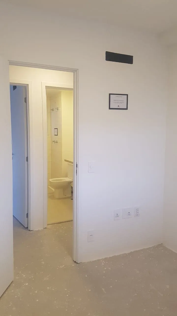 Quarto vazio com porta abrindo para o banheiro e pontos elétricos expostos, piso de contrapiso, antes da reforma