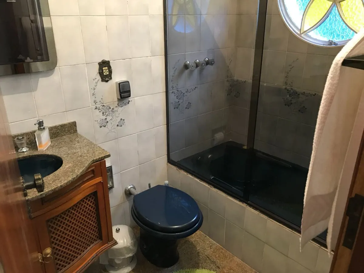 Banheiro com banheira e vaso azuis, azulejo com faixa floral e gabinete de madeira, antes da reforma