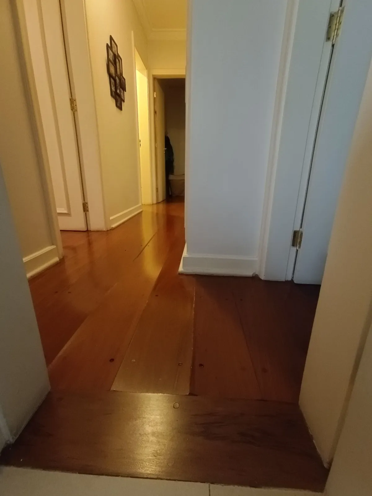 Corredor com piso de tábua corrida avermelhada gasta e portas brancas, antes da reforma