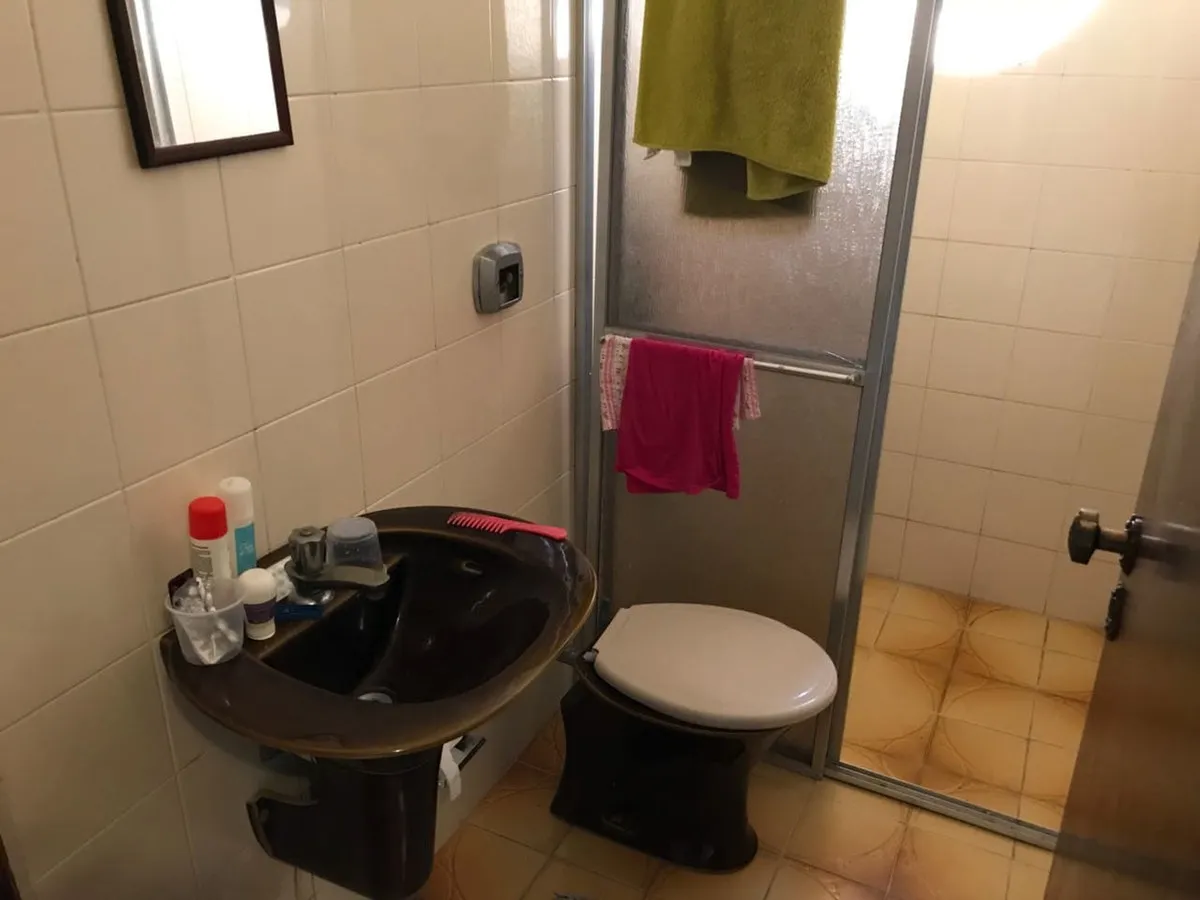Banheiro pequeno com pia e vaso marrons, azulejo branco e piso cerâmico alaranjado, antes da reforma