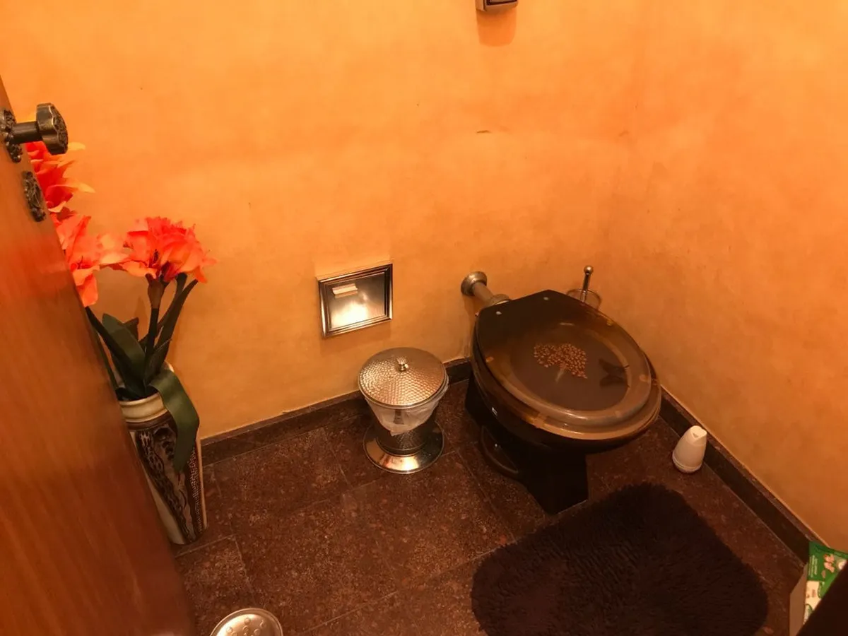 Lavabo com parede alaranjada, vaso marrom, piso de granito escuro e acessórios prateados, antes da reforma