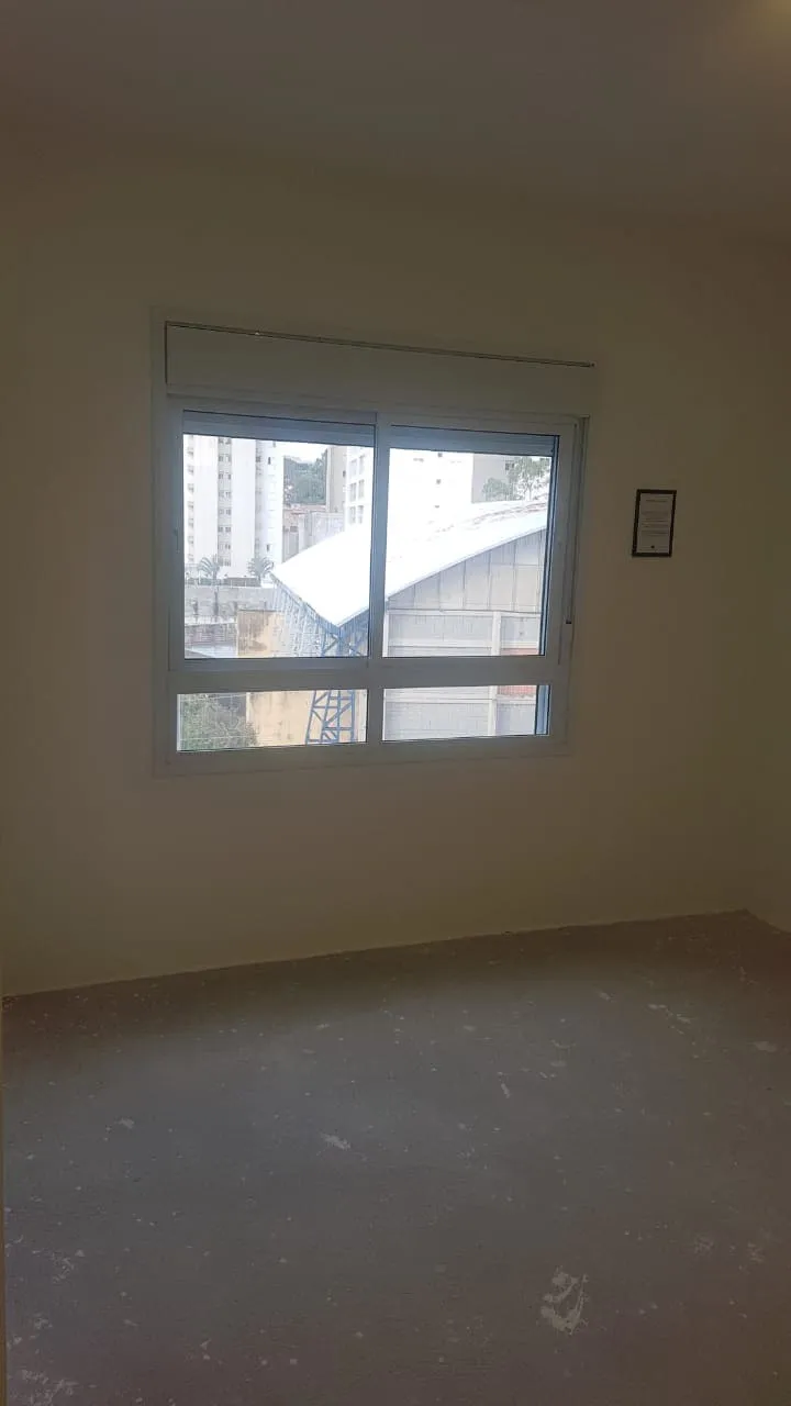 Quarto vazio de paredes claras com janela voltada para a vizinhança e piso de contrapiso cru, antes da reforma