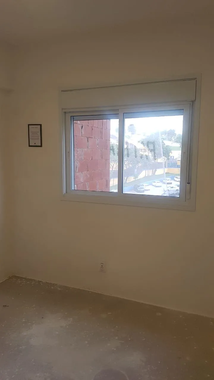 Quarto vazio com janela mostrando a parede de tijolo vizinha e piso de contrapiso, antes da reforma