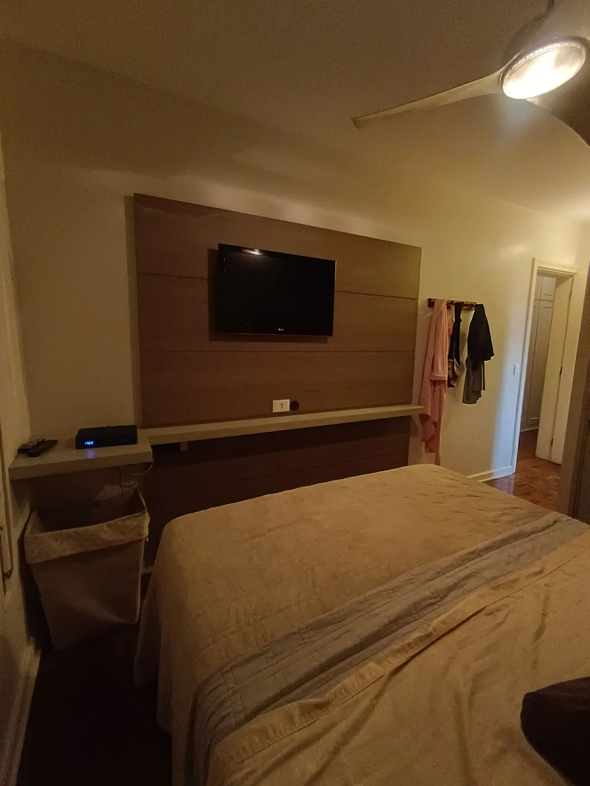 Quarto de casal com painel amadeirado, TV, bancada suspensa e piso de taco, antes da reforma