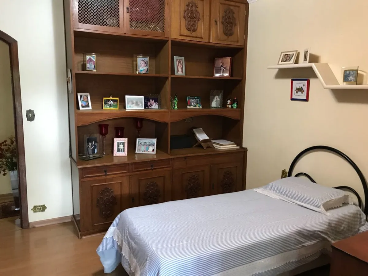 Quarto de solteiro com estante de madeira entalhada cheia de porta-retratos e cama listrada, antes da reforma