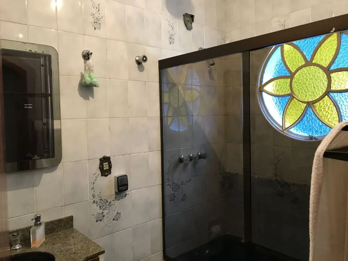 Banheiro de azulejo com faixa floral, box de vidro fumê e janela redonda de vitral colorido, antes da reforma