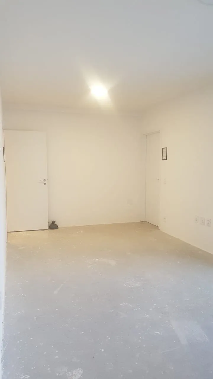 Sala vazia de paredes brancas com duas portas e piso de contrapiso cinza, antes da reforma