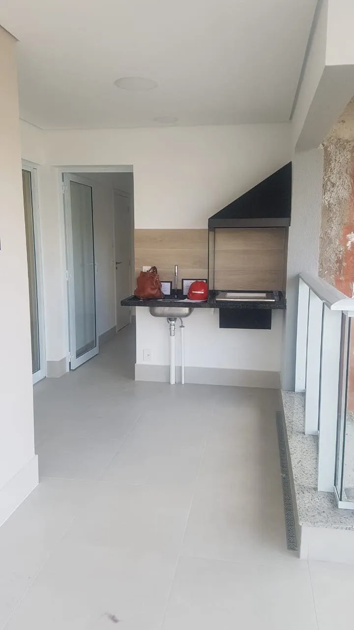 Varanda gourmet original com churrasqueira, coifa preta e bancada de granito com cuba, piso porcelanato claro, antes da reforma