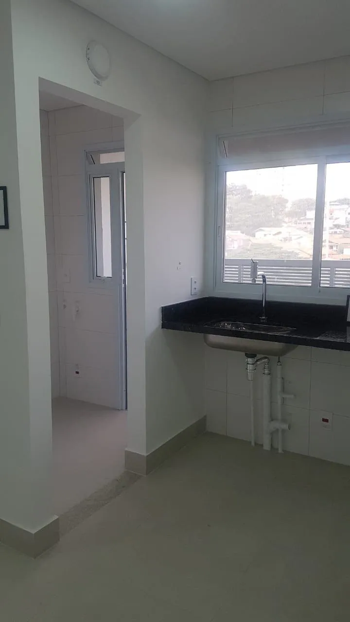 Cozinha pequena e fechada com bancada de granito preto, cuba de inox e passagem para a área de serviço, antes da reforma