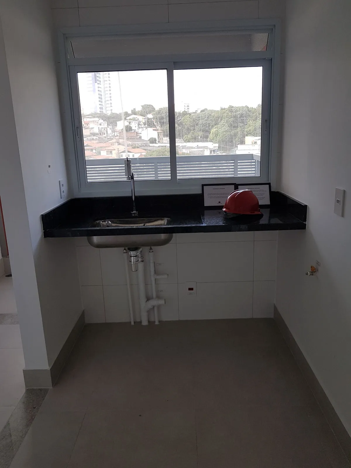 Cozinha estreita com bancada de granito preto, cuba de inox e janela com vista da cidade, antes da reforma