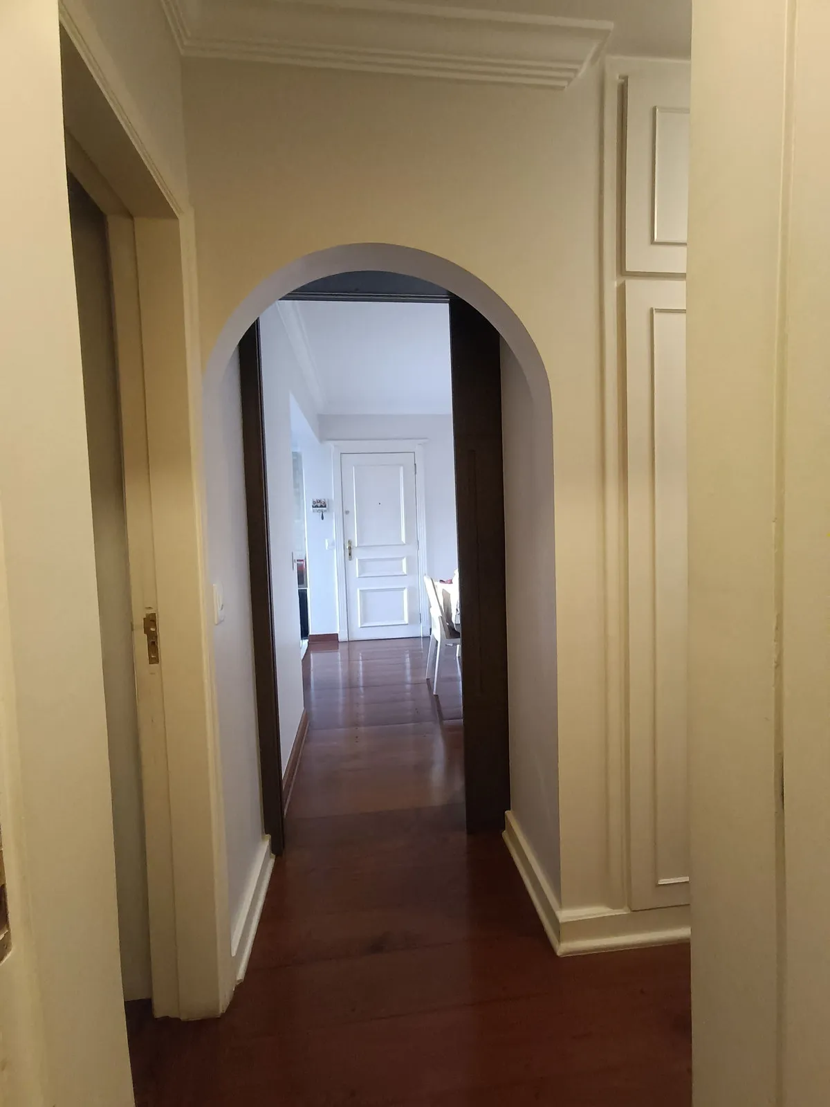 Corredor com arco de passagem, portas brancas almofadadas e piso de tábua corrida avermelhada, antes da reforma