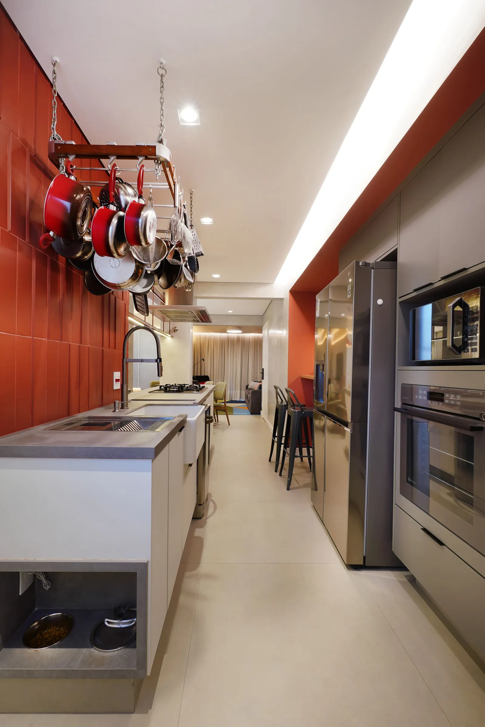 Cozinha corredor com azulejo laranja, varal de panelas, geladeira inox e forno embutido, aberta para a sala