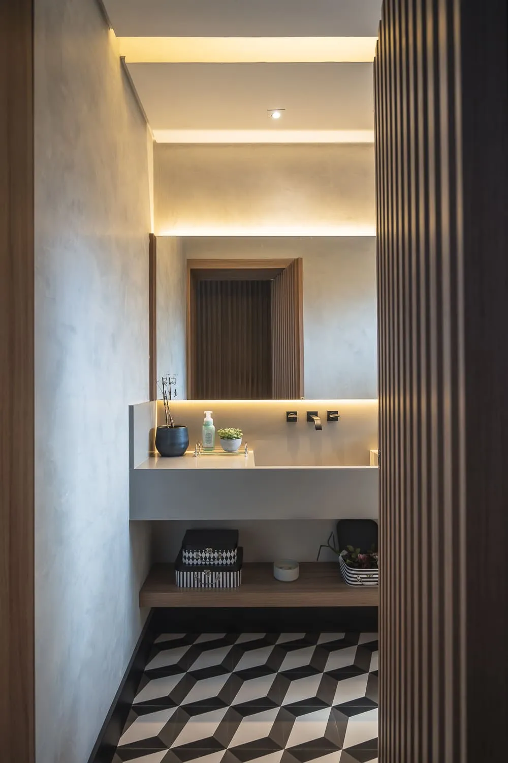 Lavabo com cuba branca suspensa, espelho iluminado, parede ripada e piso de ladrilho geométrico preto e branco