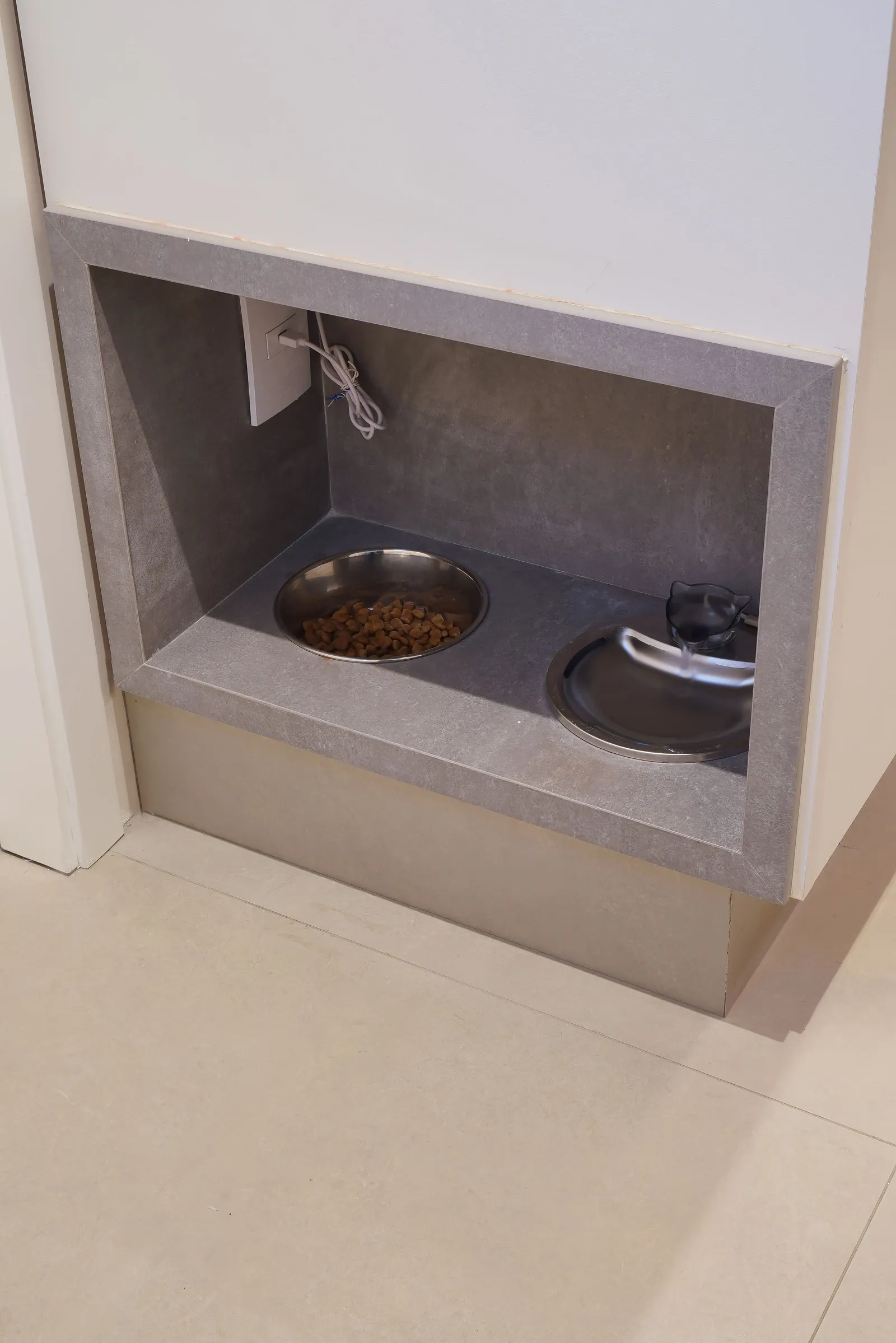 Nicho de alimentação dos pets em pedra cinza, com comedouro de inox e bebedouro-fonte no nível do piso