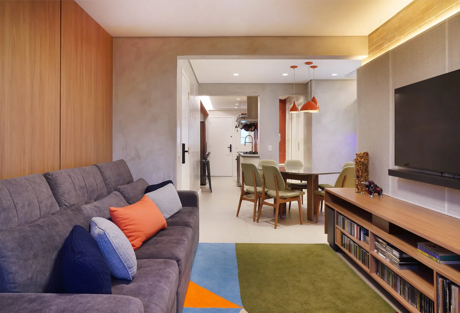 Sala de estar integrada ao jantar, com sofá cinza, tapete geométrico e mesa com cadeiras verdes ao fundo