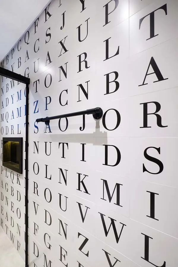 Detalhe da parede de revestimento com letras estilo caça-palavras, barra de toalha preta e nicho, no banheiro
