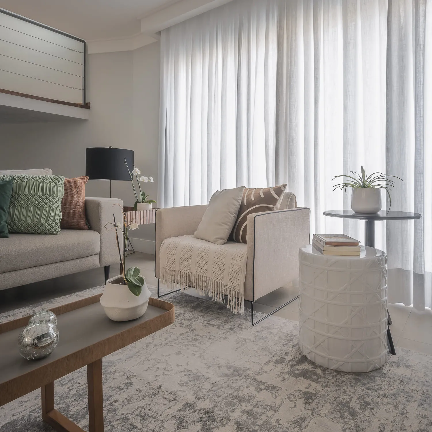 Estar com poltrona bege de tricô, mesa lateral de cerâmica branca e cortinas de linho até o chão