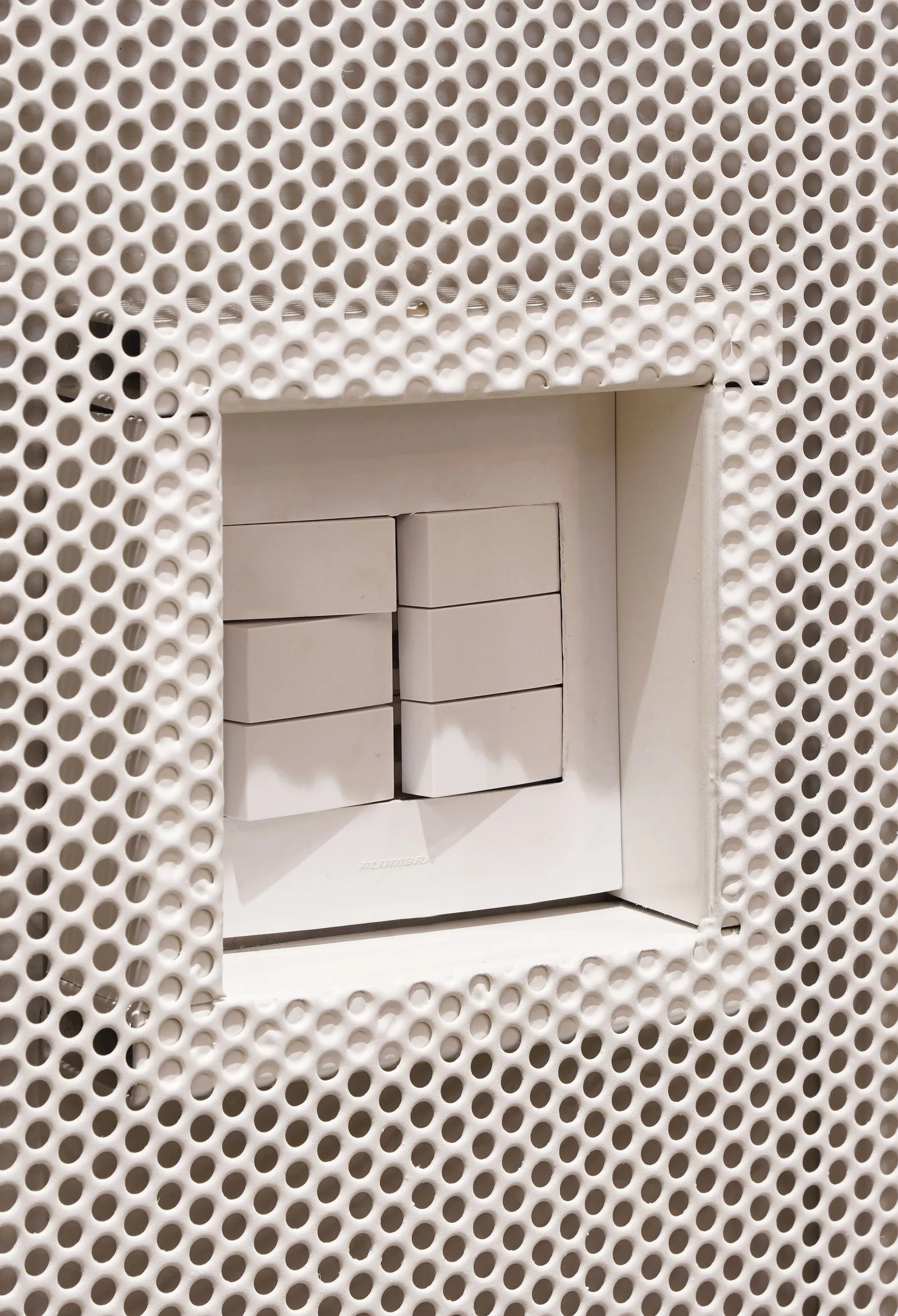 Detalhe do painel de metal perfurado branco, com os interruptores embutidos num recorte quadrado