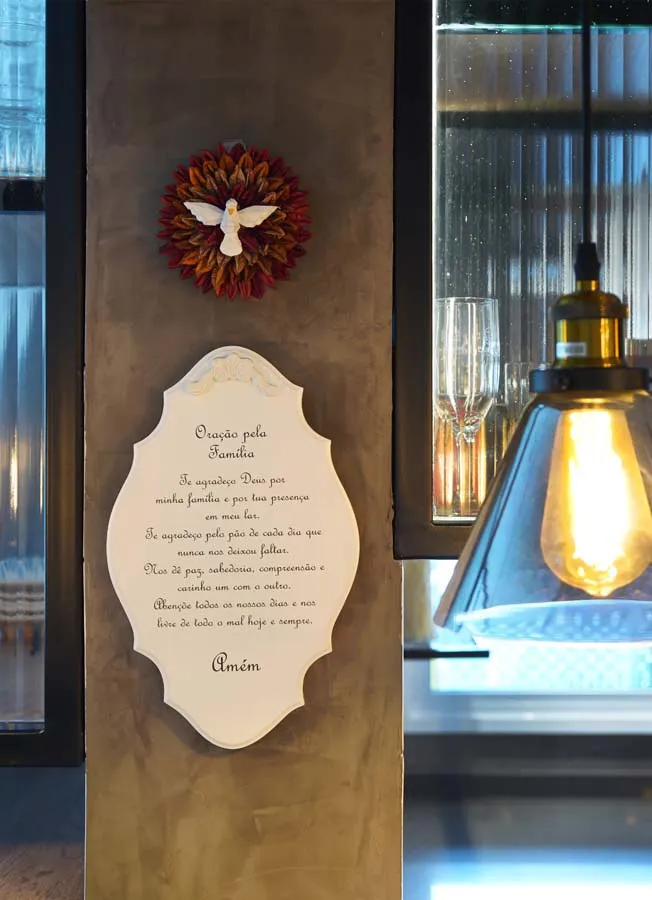 Detalhe da coluna de cimento queimado com o quadro da Oração pela Família e o divino, ao lado de pendente de vidro âmbar e parede de vidro canelado