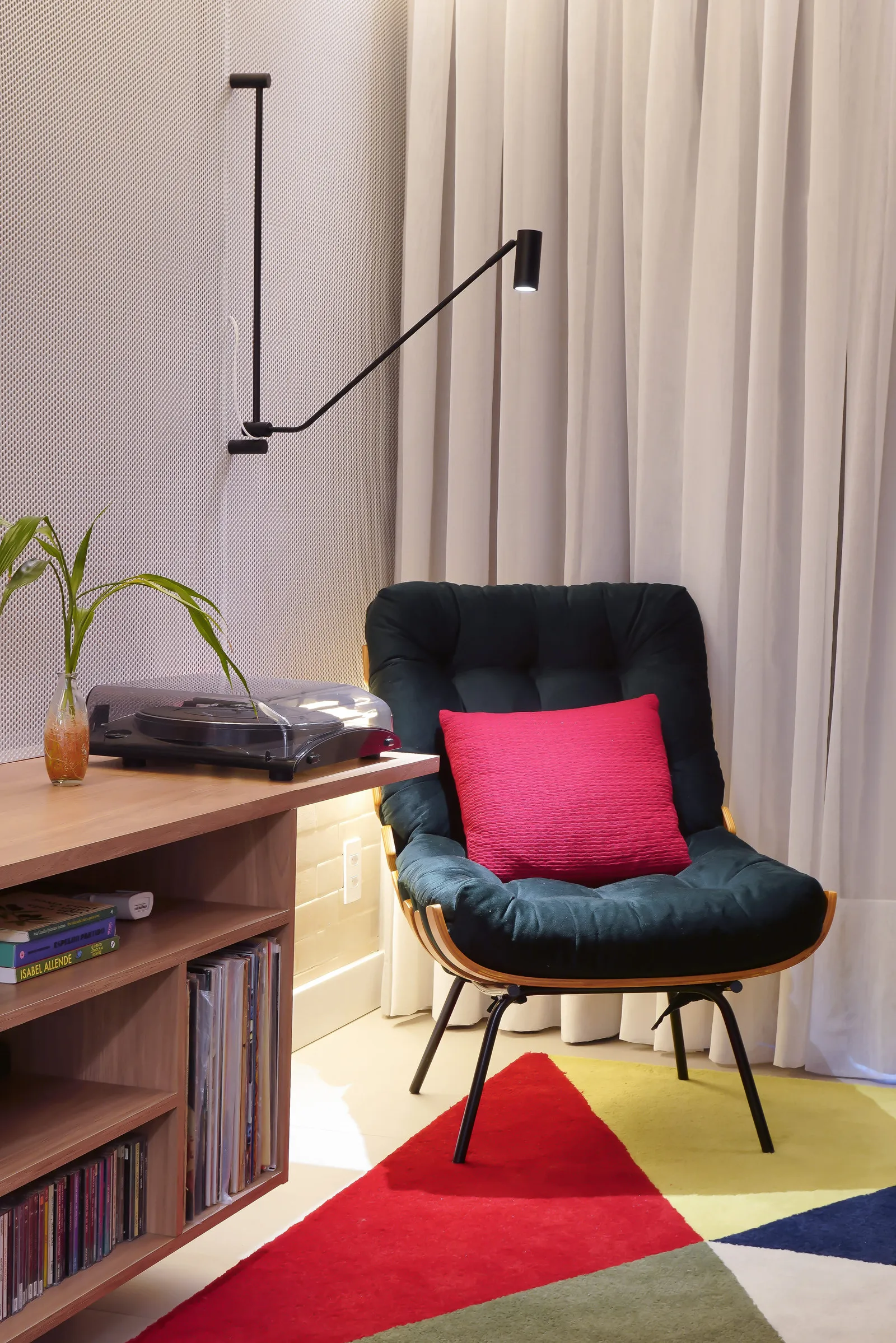 Canto de leitura com poltrona Costela preta e almofada rosa, luminária articulada preta e rack com toca-discos