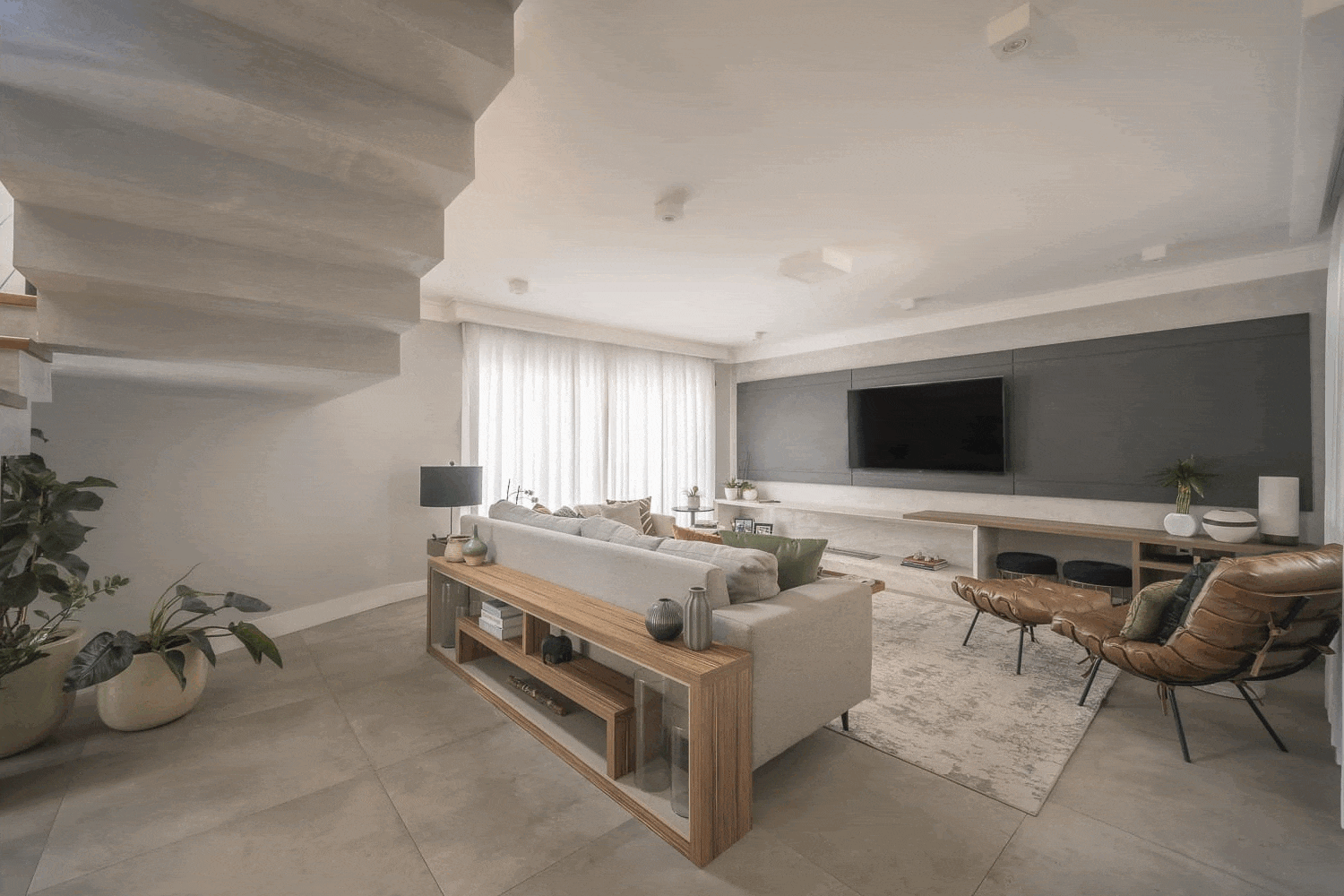 Sala de estar com aparador de madeira atrás do sofá, escada de concreto ao fundo e piso de porcelanato cimentício